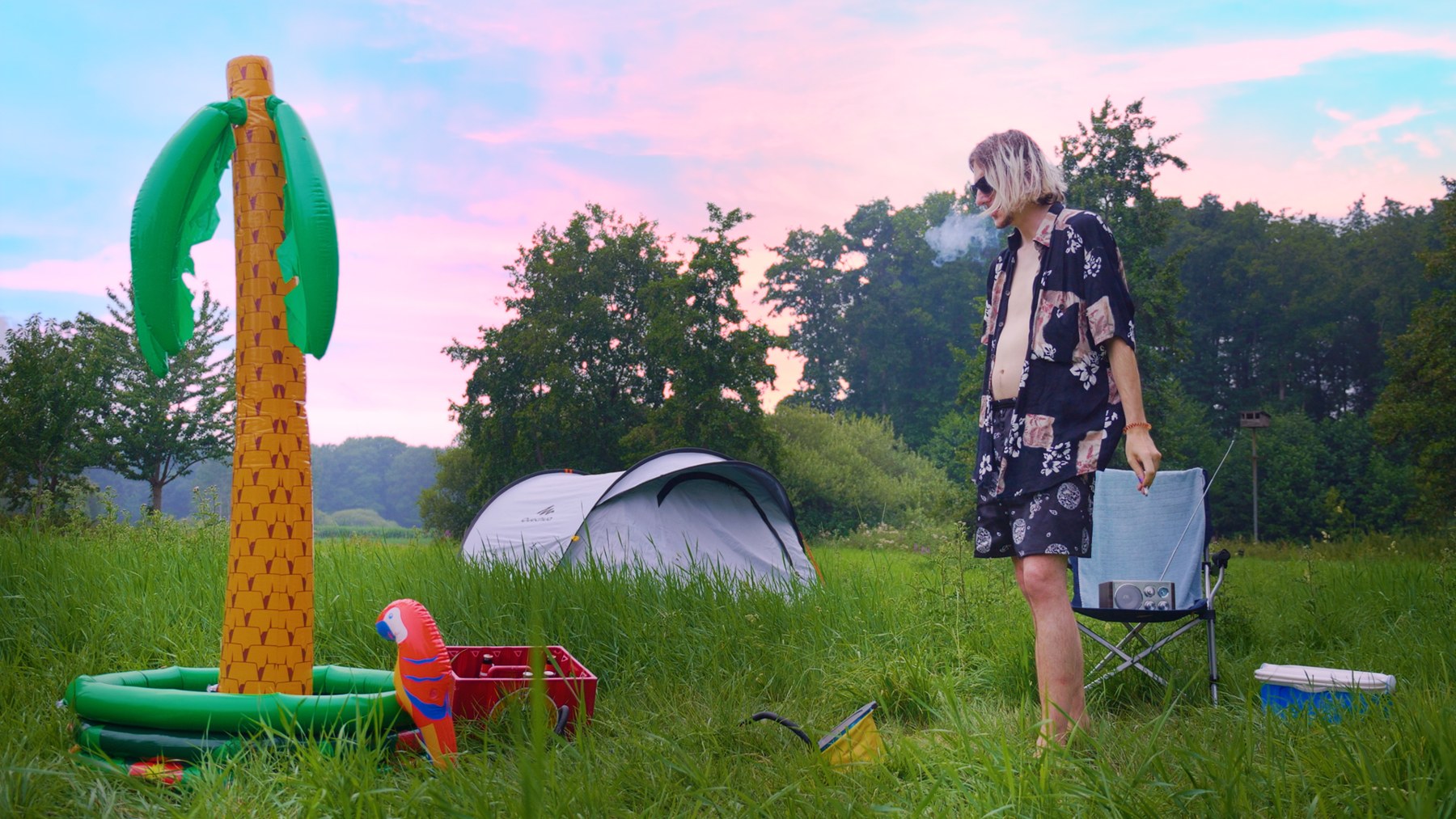 A lone figure and a tall inflatable plastic palm tree in a summer field.